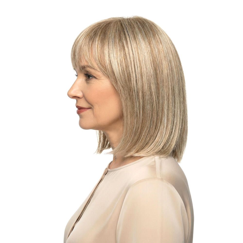 Blond gefärbte Perücke mit Pony. Mittellange, gestufte Haare. Frau mit hellem Oberteil. Seitenansicht.