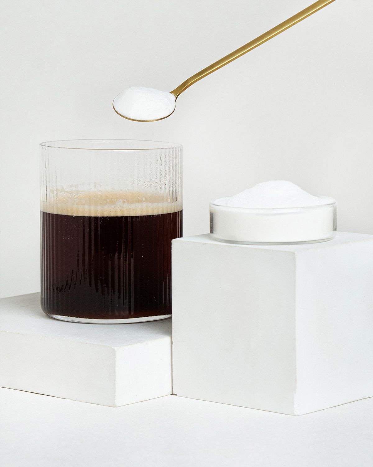 Ein Glas Kaffee, ein Löffel MCT-Öl Pulver und eine Schale Pulver.