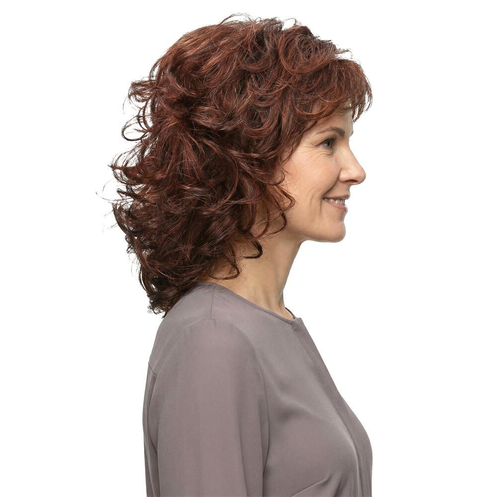Profil einer lächelnden Frau mit rotbrauner, gewellter Perücke. Graues Oberteil. Heller Hintergrund.