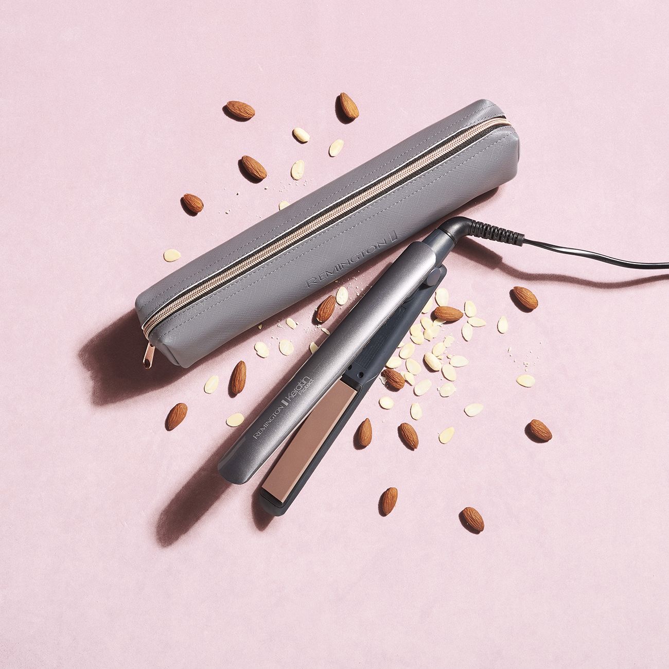 Glätteisen mit Keratin-Technologie und grauer Aufbewahrungstasche. Mandeln auf rosa Untergrund.