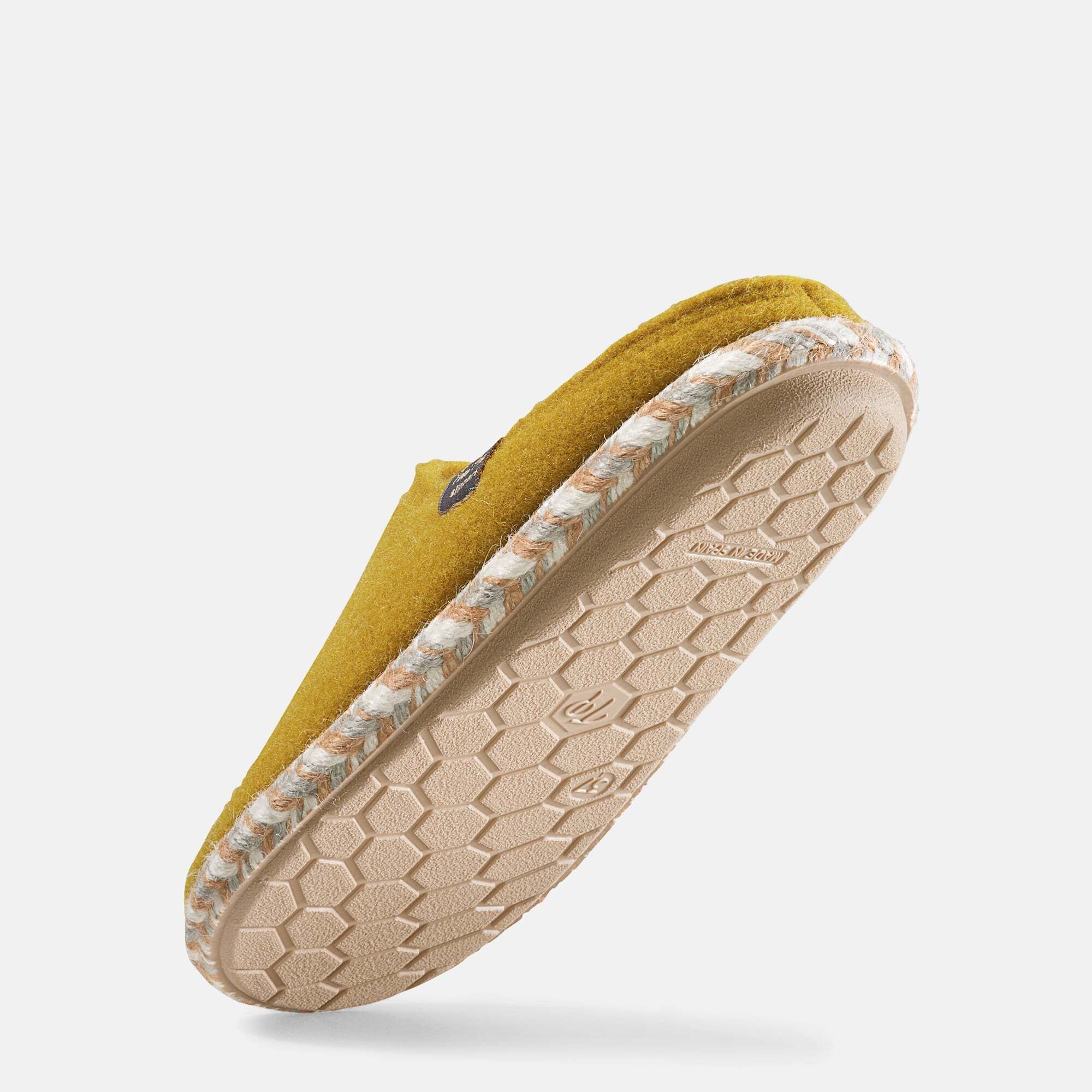 Senffarbener Hausschuh mit weißem Innenfutter und geflochtener Sohle. Label mit Schriftzug. Unterseite der Sohle sichtbar.