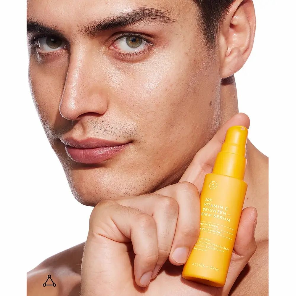 Mann hält gelbe Flasche mit Serum. Text: 20% Vitamin C Brighten + Firm Serum. Marke: ALLIES OF SKIN.