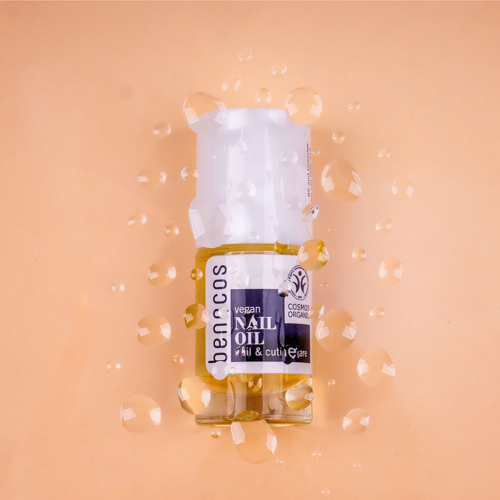 Benecos vegan Nail Oil Fläschchen umgeben von Wassertropfen auf einem hellen Hintergrund. Für Nagel- und Nagelhautpflege.