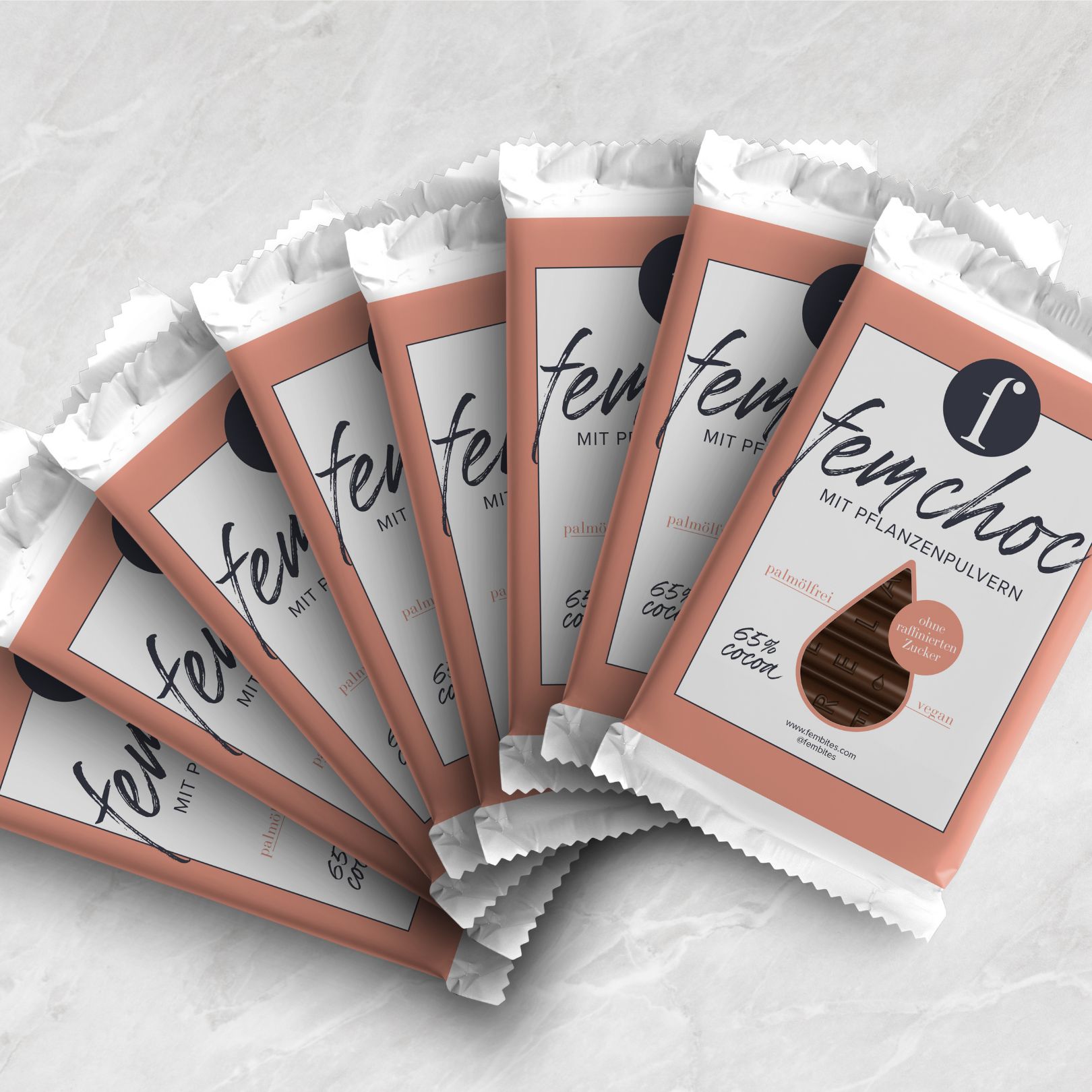 Mehrere verpackte Schokoriegel, fächerförmig angeordnet. Logo und Schriftzug 'fembites femchoc'. Text: 65% Kakao.