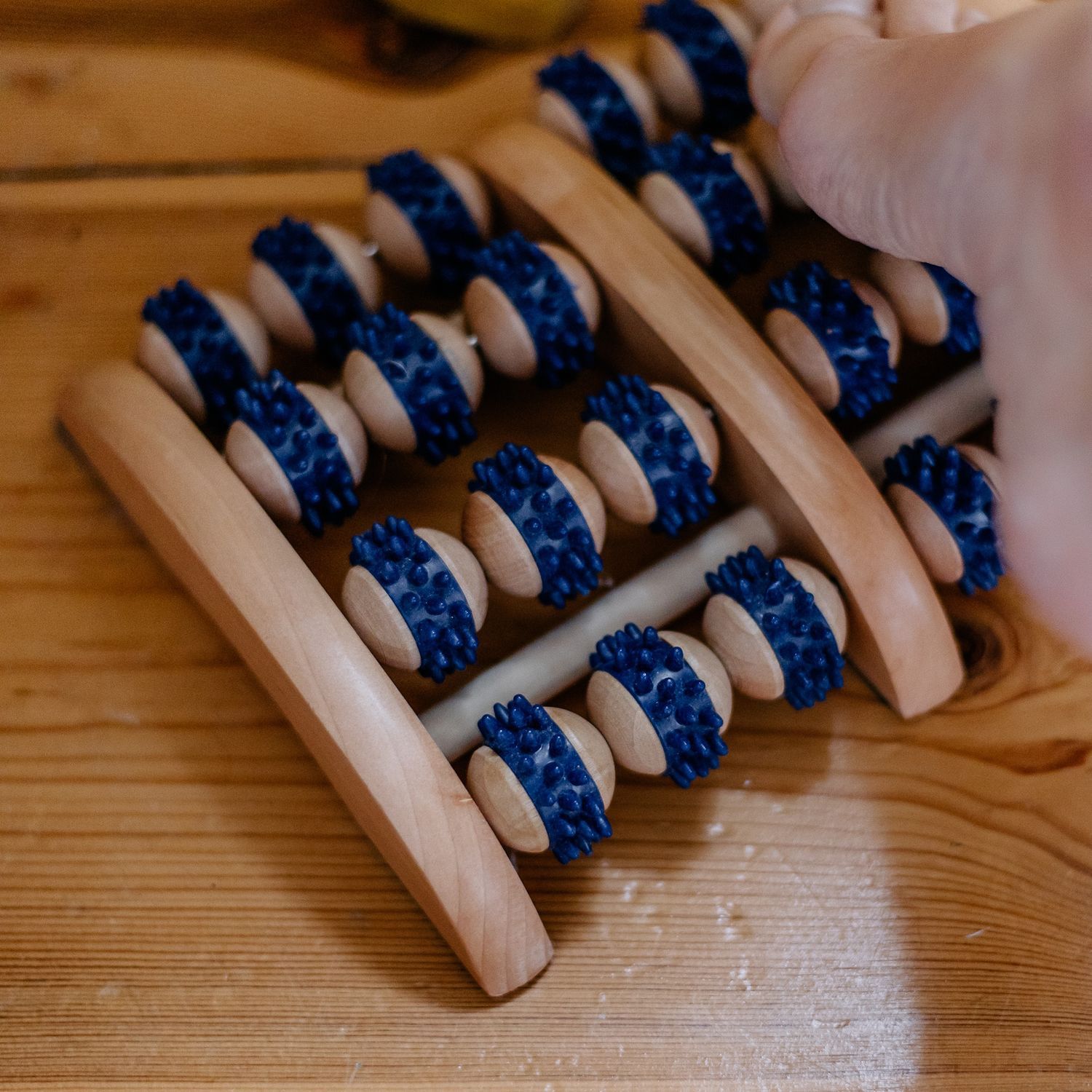Holz-Fußmassagegerät mit 2 Reihen à 4 Rollen, eine Hand benutzt es.