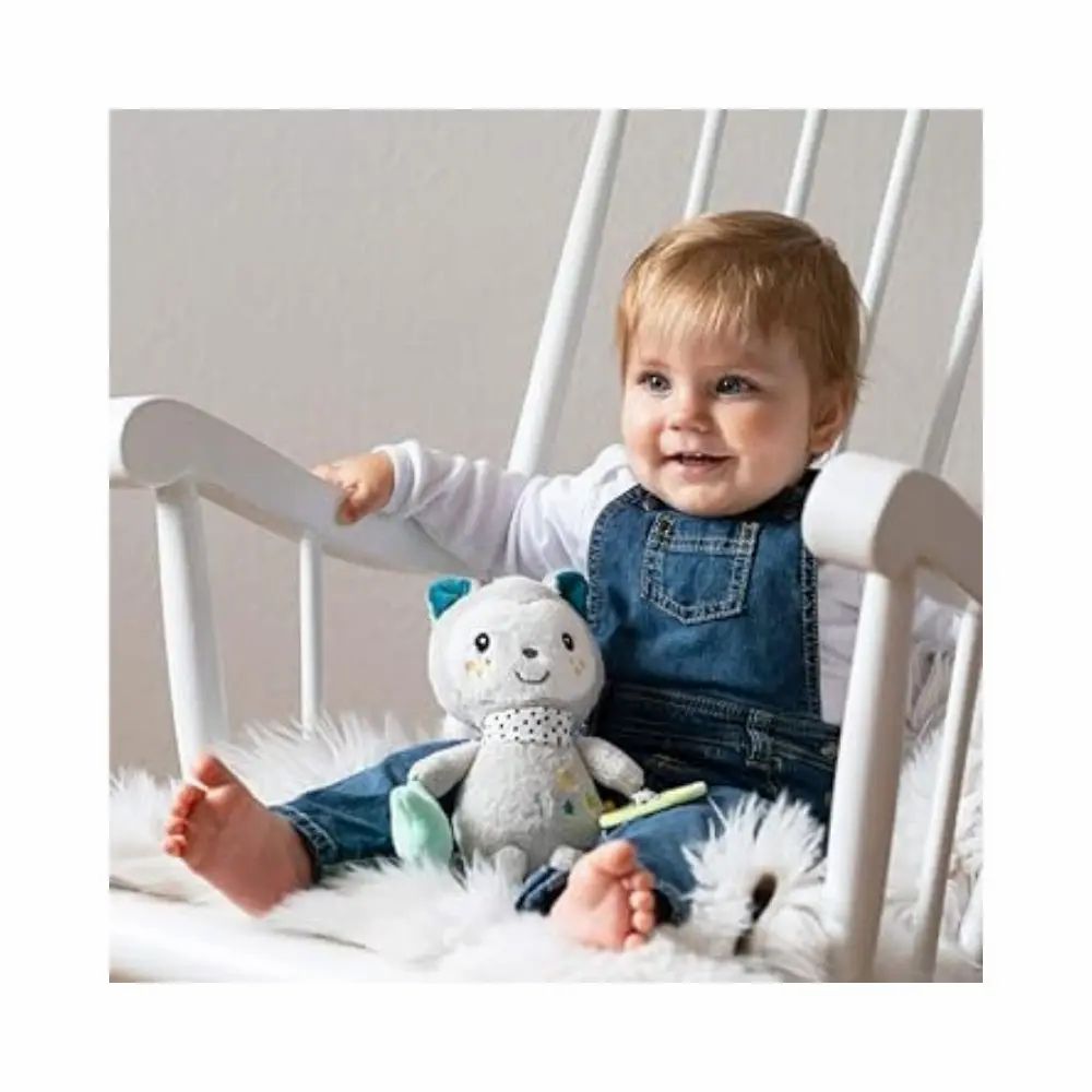 Baby sitzt auf Schaukelstuhl und hält graues Kuscheltier. Kuscheltier hat blaue Ohren, gepunkteten Schal, Stern, Spiegel und Rassel.