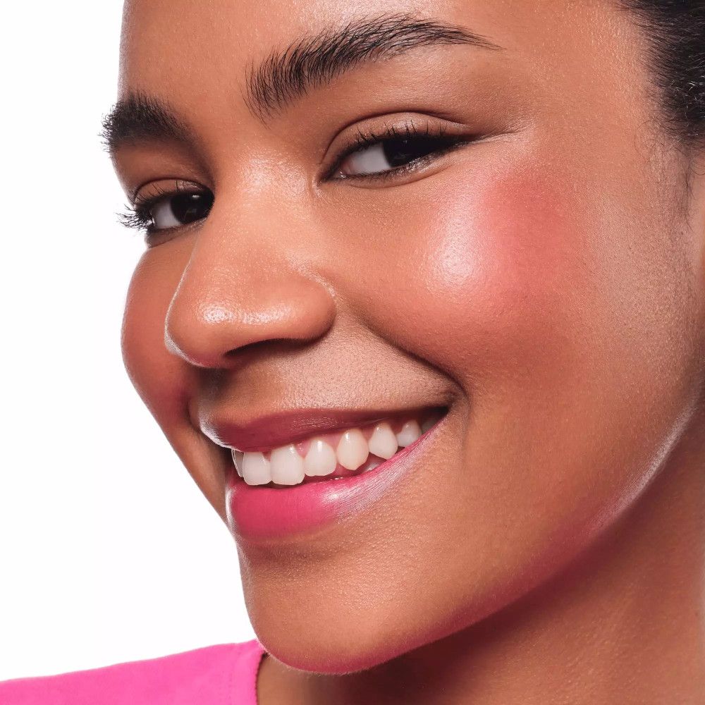 Nahaufnahme eines lächelnden Gesichts. Gebräunte Haut mit rosa Wangen und Lippen. Dunkle Haare, Augenbrauen und Wimpern.