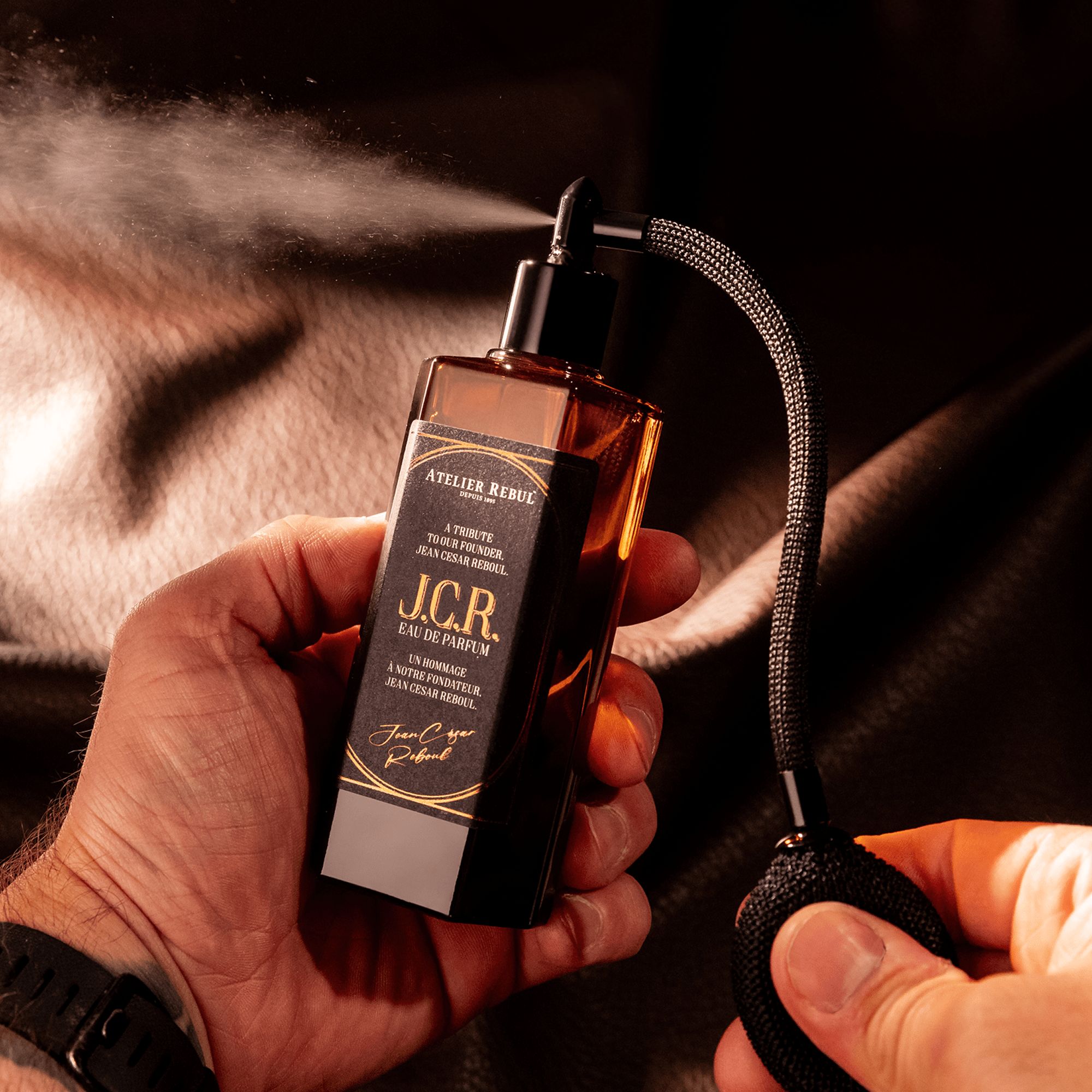 Braune Glasflasche mit schwarzem Zerstäuber. Sprühnebel. Aufschrift: Atelier Rebul J.C.R. Eau de Parfum.
