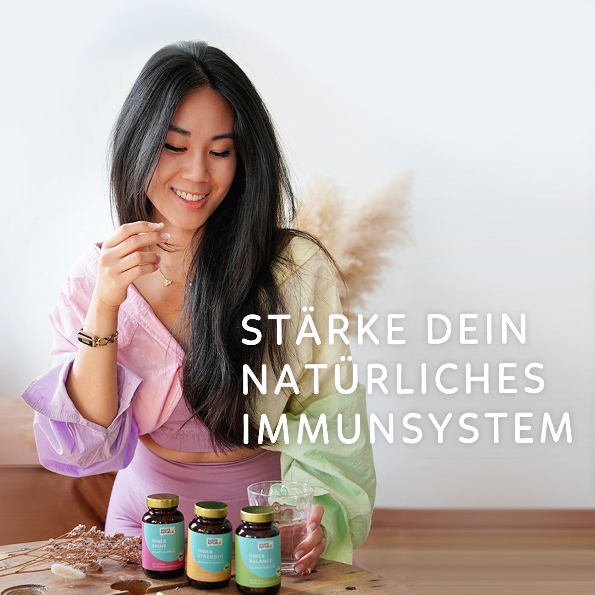 Frau hält Kapsel, vor ihr stehen Flaschen. Aufschrift: Shape Republic, Inner Strength, Immunity Komplex.