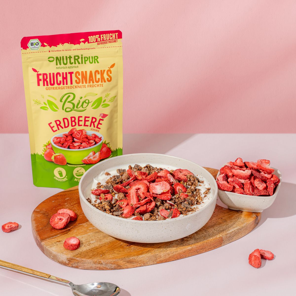 Verpackung NutriPur FruchtSnacks Bio-Erdbeere, Schale mit Erdbeeren und Müsli, Schale mit Erdbeeren, Holzbrett, Löffel.