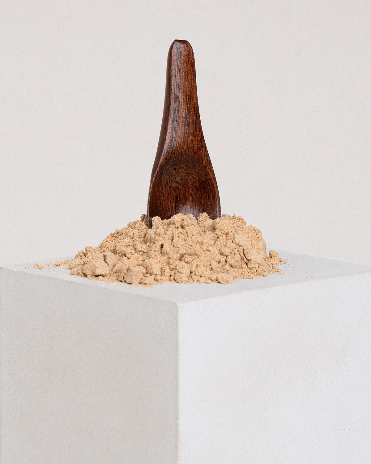 Beige Pulver auf weißem Podest, Holzschaufel steckt darin.