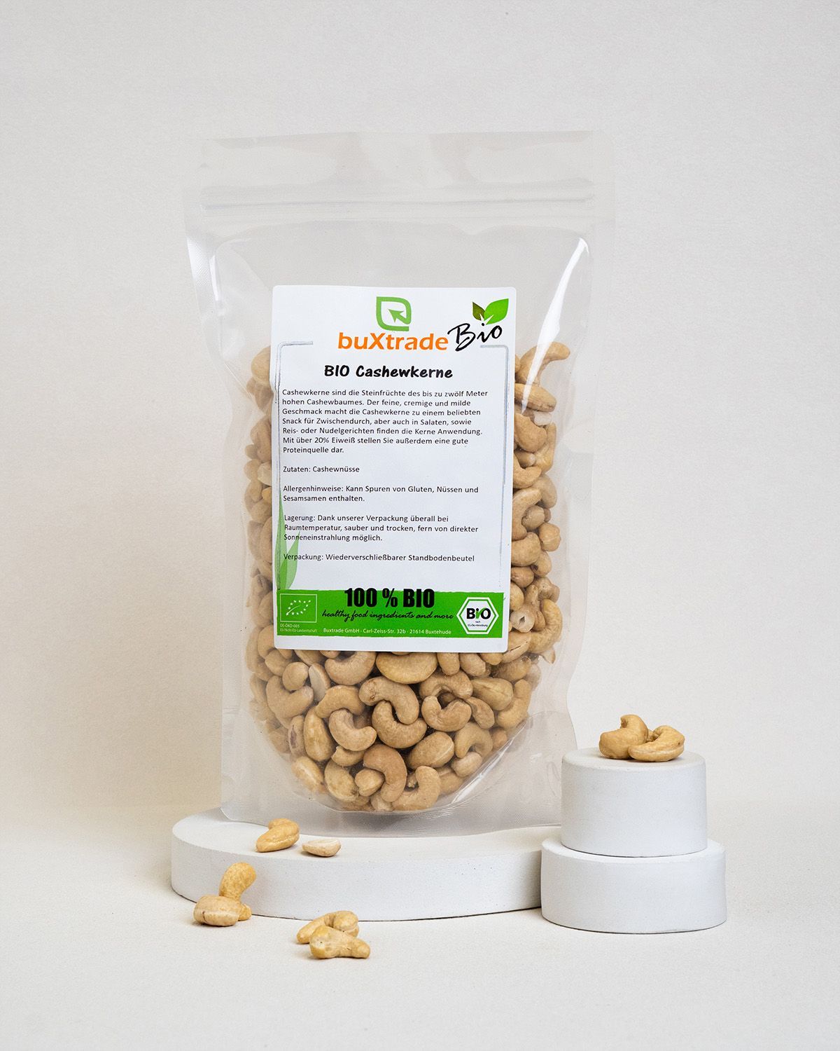 Transparente Verpackung mit buXtrade Bio Cashewkernen auf Podest. Etikett mit Produktinfo und Bio-Siegel.