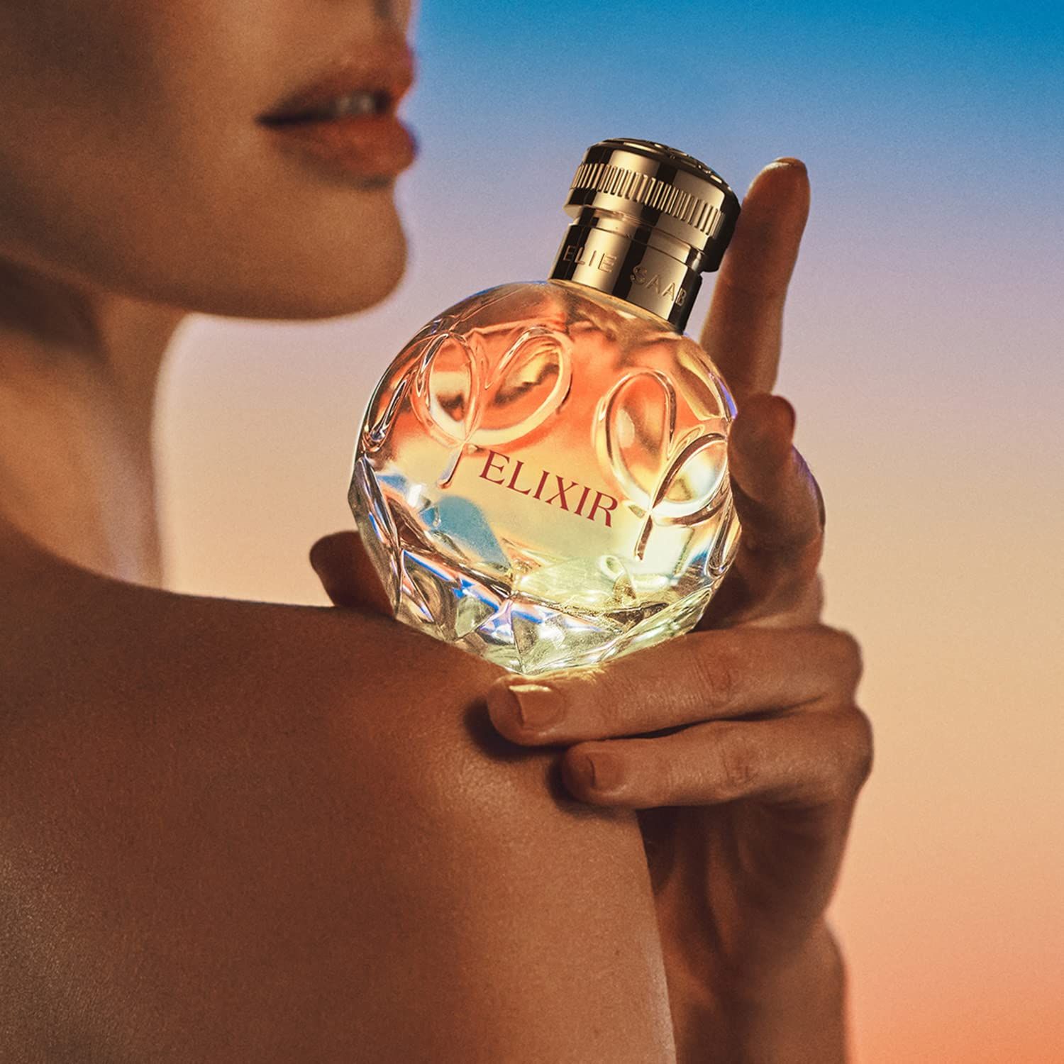 Nahaufnahme einer Frau, die einen Flakon hält. Runder Flakon mit goldfarbenem Verschluss. Aufschrift "ELIXIR".