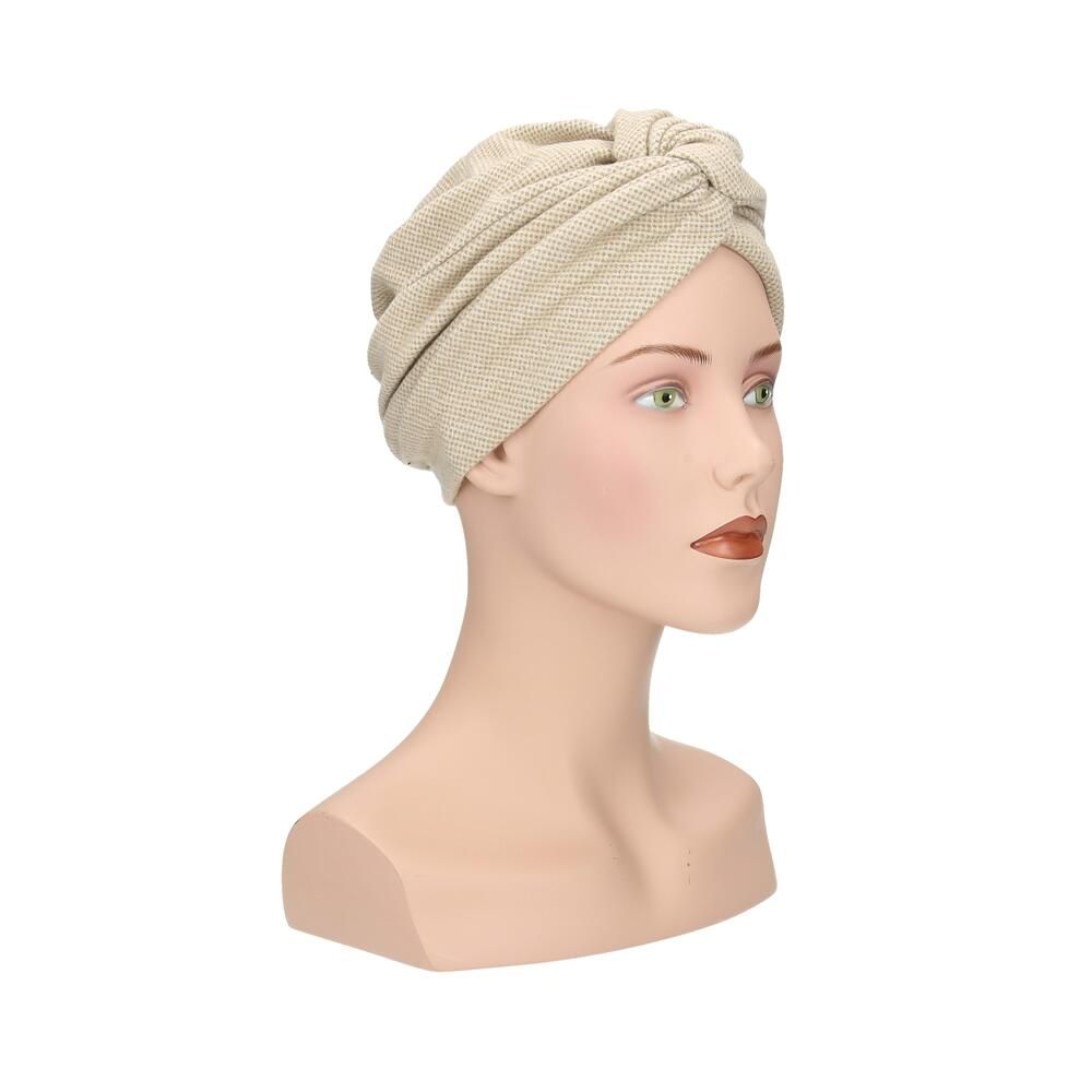 Beigefarbener Turban aus Stoff mit Knoten vorne, auf einer Schaufensterpuppe.