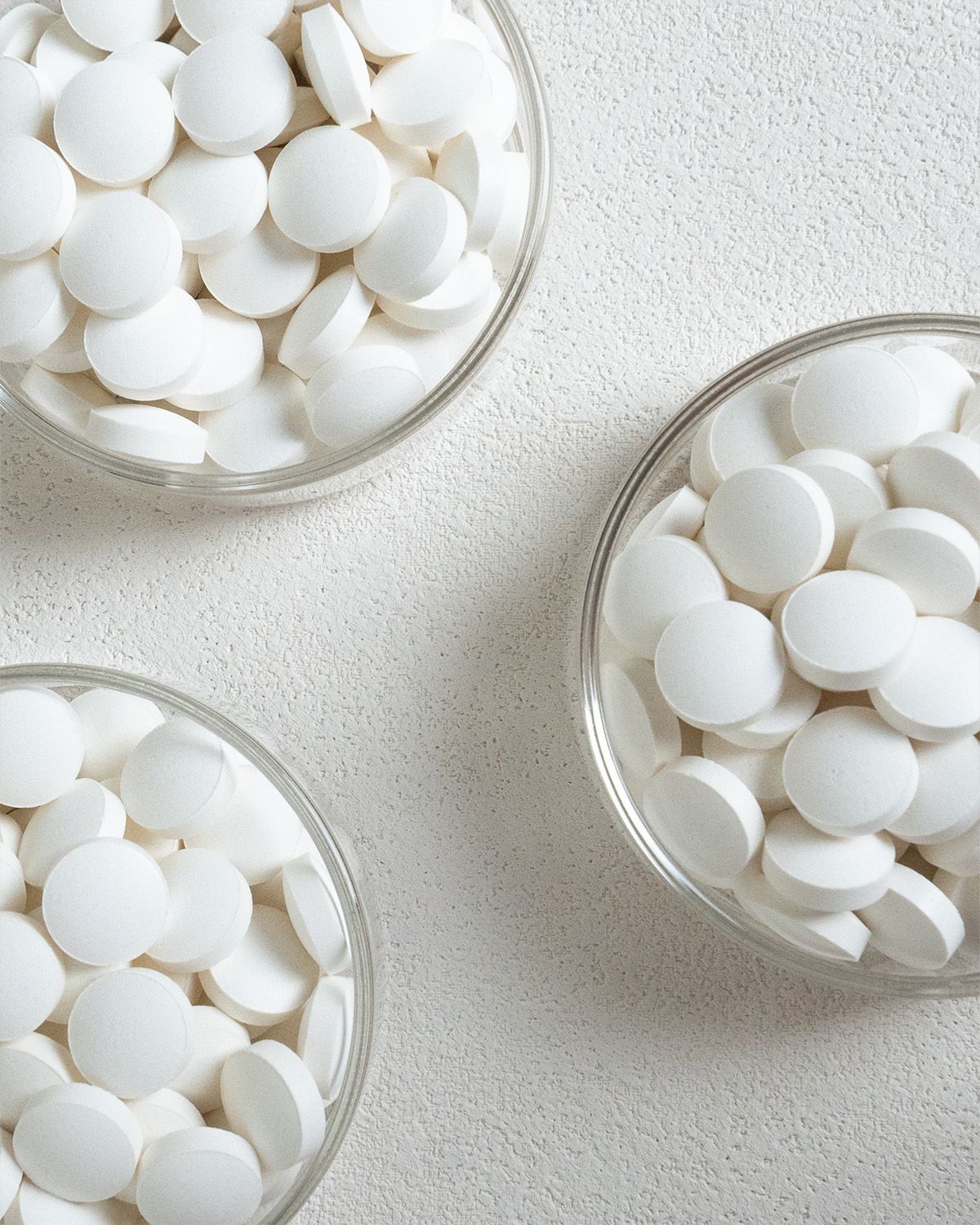Drei Gläser mit Zinkbisglycinat Tabletten auf weißem Untergrund.