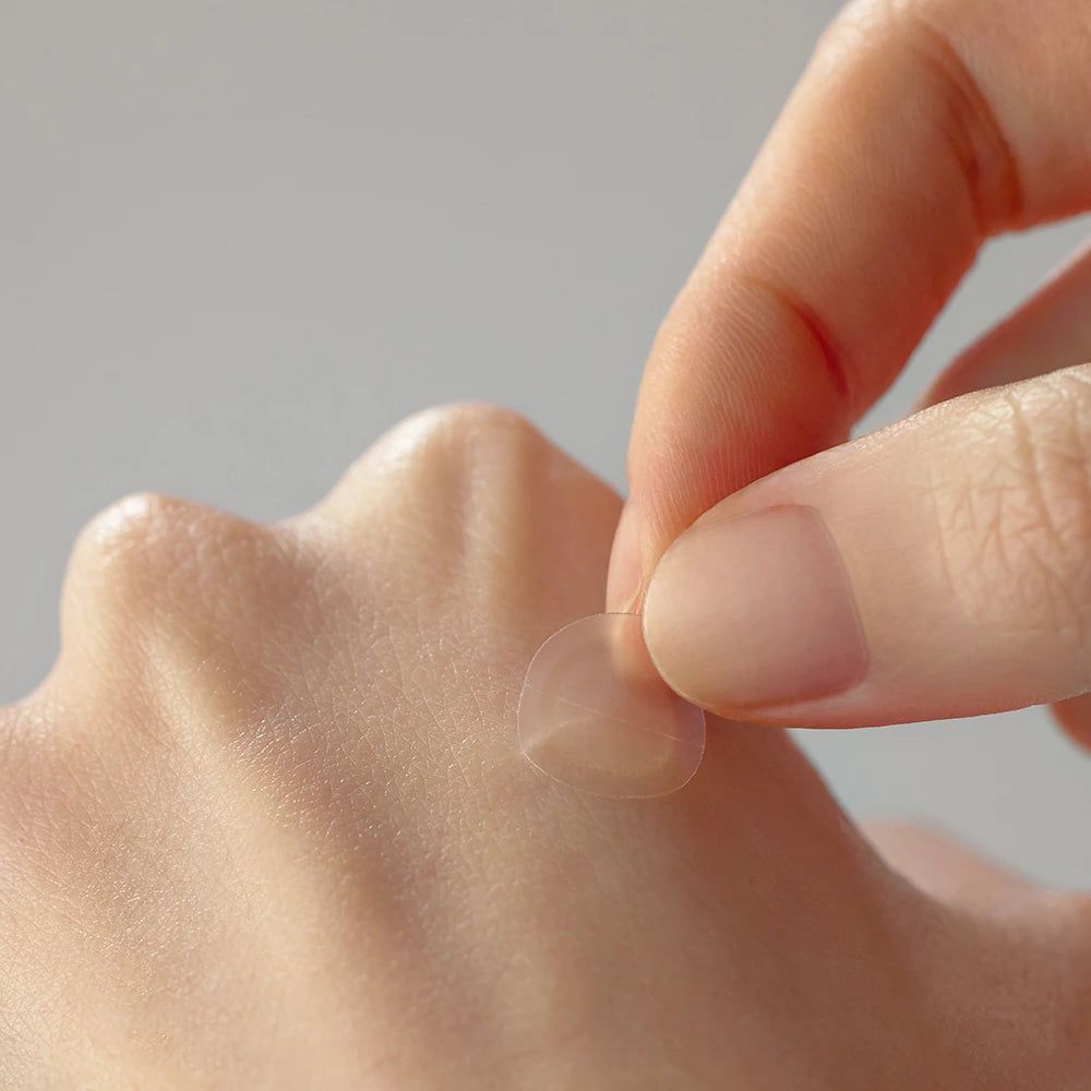 Eine Hand platziert einen transparenten, runden Patch auf der Haut.