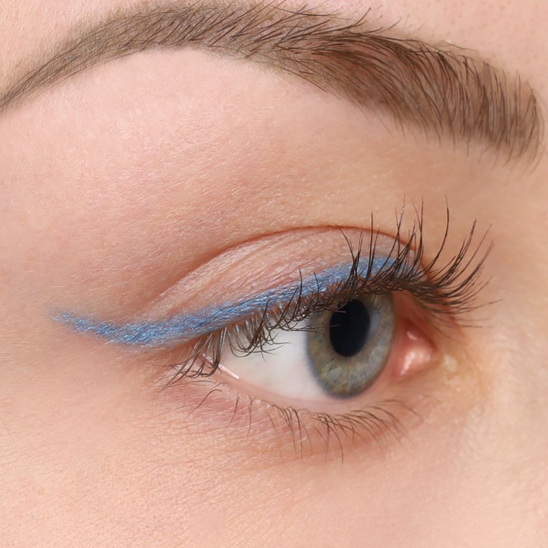 Nahaufnahme eines Auges mit blauem Kajal-Eyeliner. Die blaue Linie verläuft entlang des oberen Wimpernkranzes.