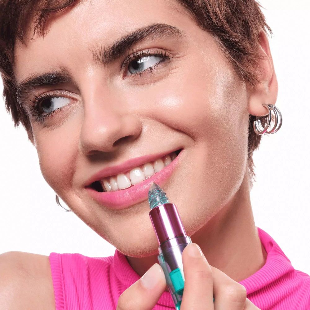 Eine Frau trägt den Aqua Jelly Lippenstift auf. Sie lächelt. Der Lippenstift ist blau und glänzend.