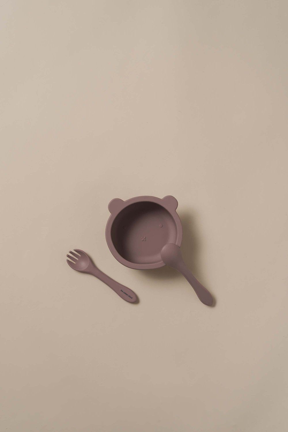 Mauve Schüssel mit Löffel und Gabel. Auf beigem Hintergrund.