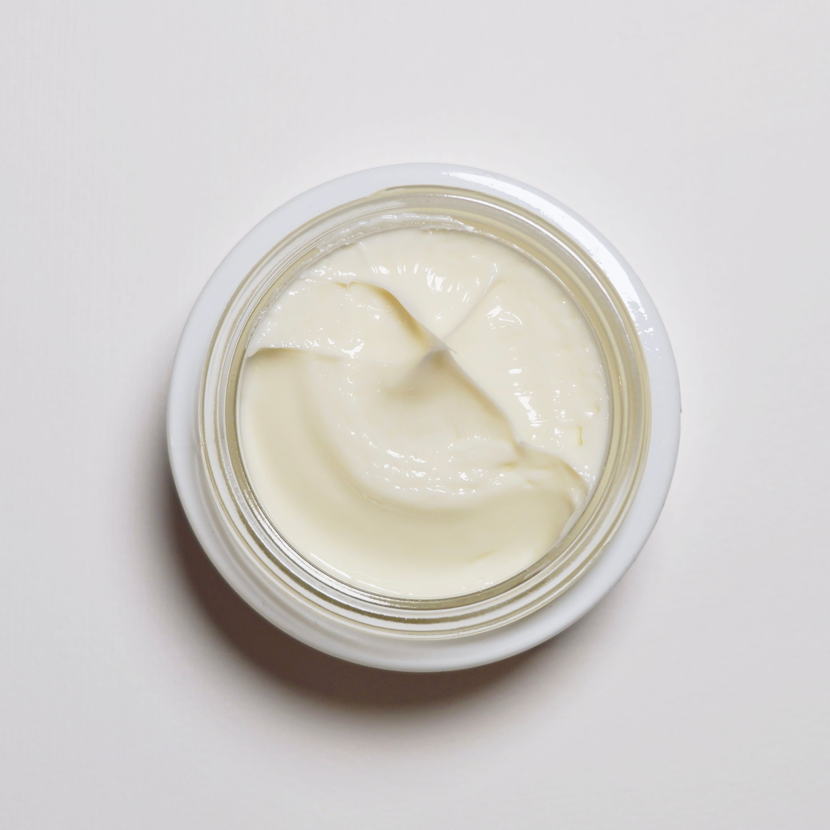 Creme in einem offenen, weißen Glas. Die Creme ist weiß und hat eine glatte Textur.