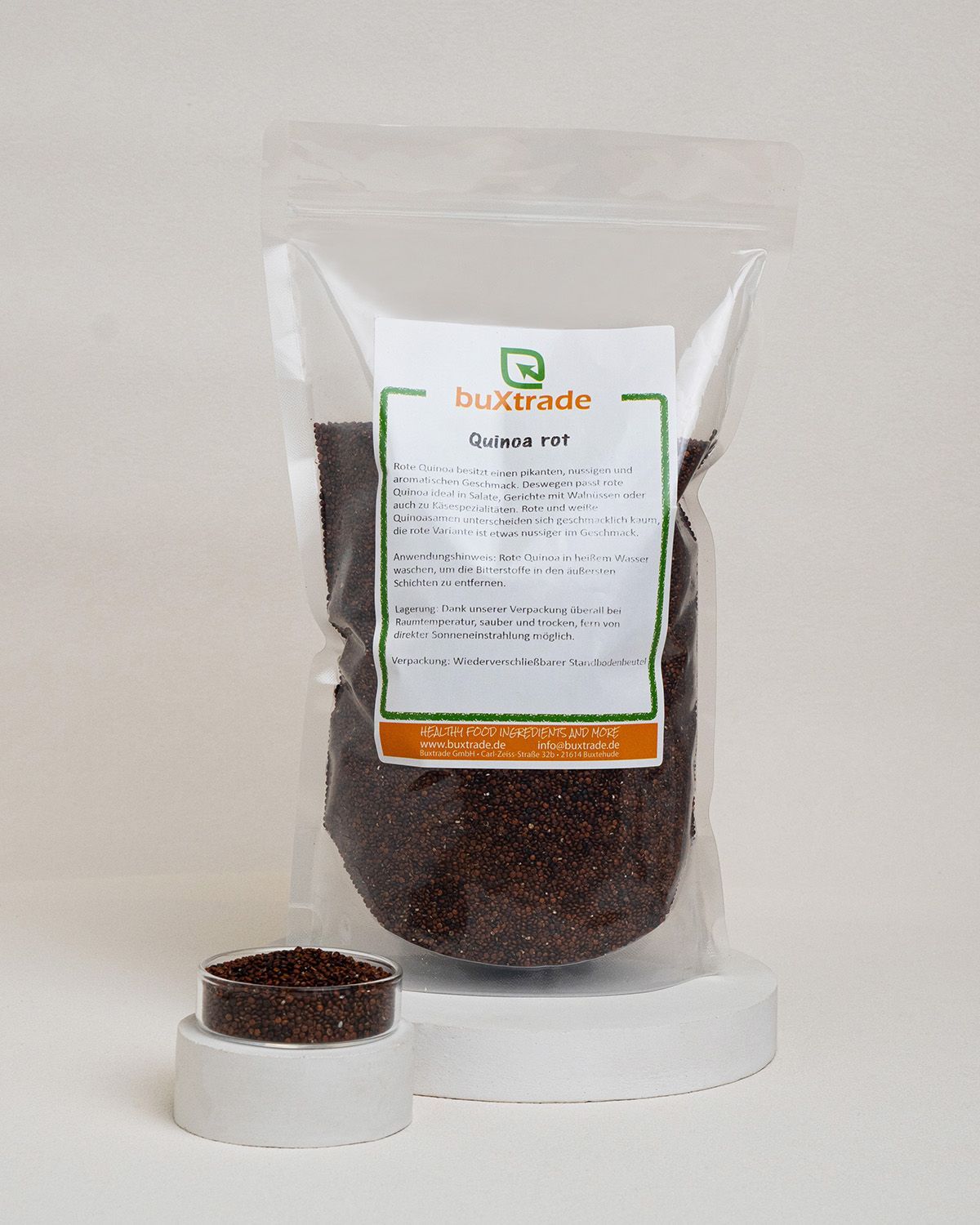 Transparente Tüte mit rotem Quinoa. Aufkleber mit Produktinformationen und Logo von buxtrade. Kleines Schälchen mit Quinoa daneben.