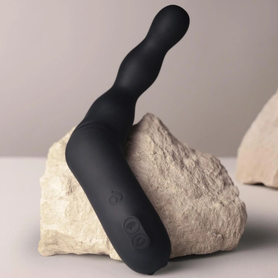 Schwarzer Vibrator auf einem Stein platziert. Länglicher Körper mit abgerundeten Enden und Bedienknöpfen.