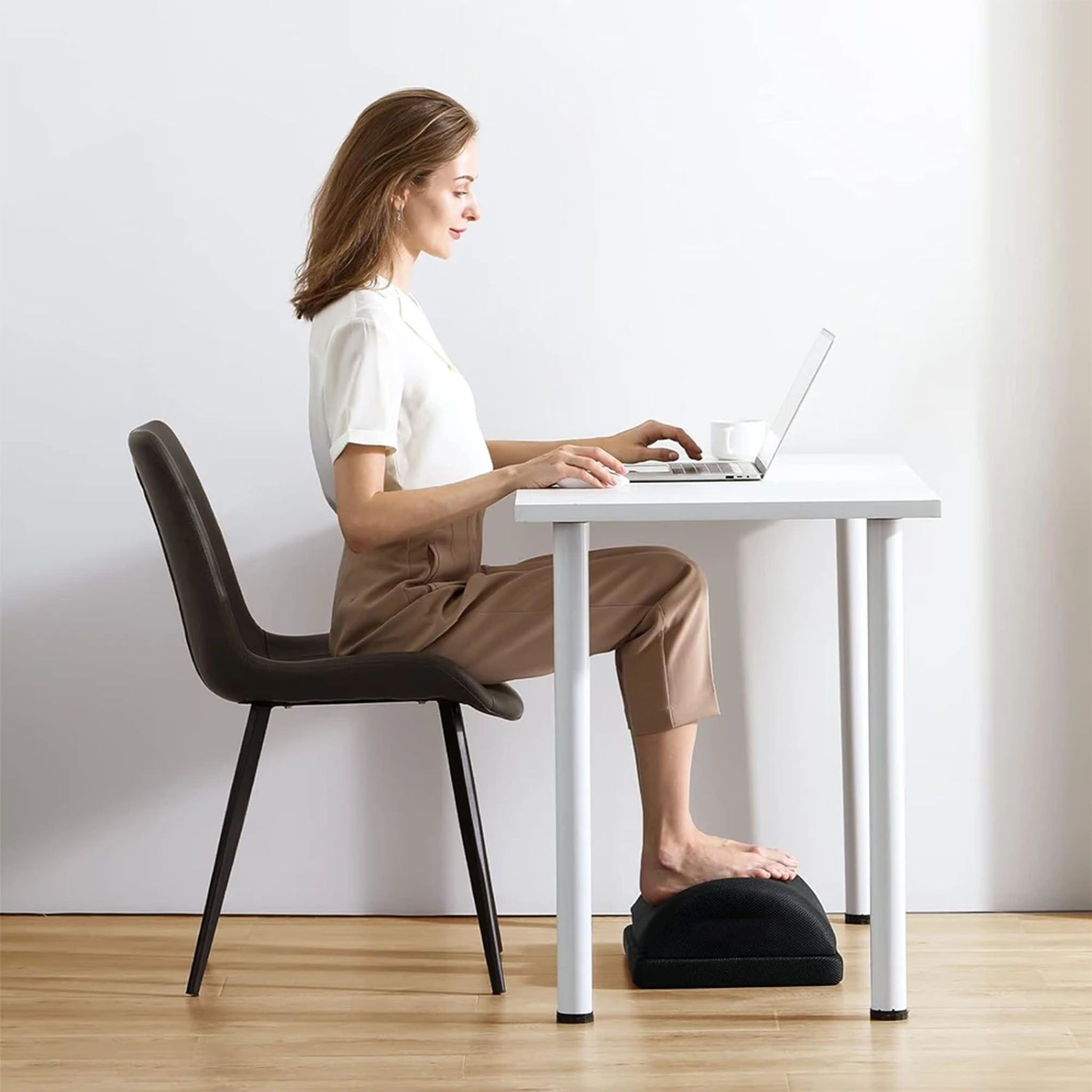 Frau sitzt am Schreibtisch, Füße auf einer ergonomischen Fußstütze.