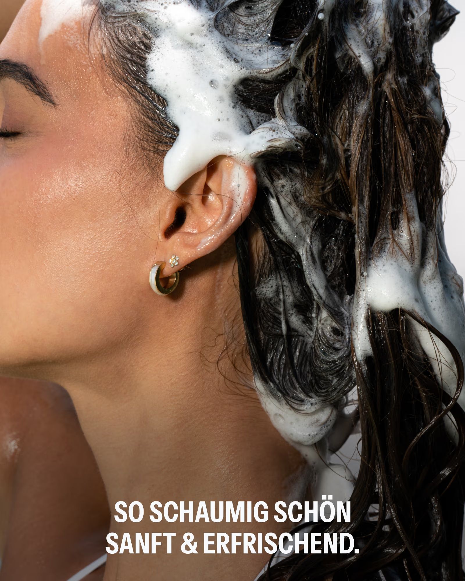 Nahaufnahme einer Frau, die sich die Haare mit schäumendem Shampoo wäscht.