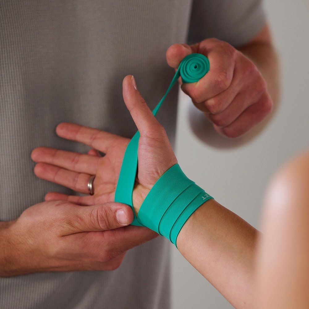Ein Mann wickelt ein grünes Flossband um das Handgelenk einer Frau.