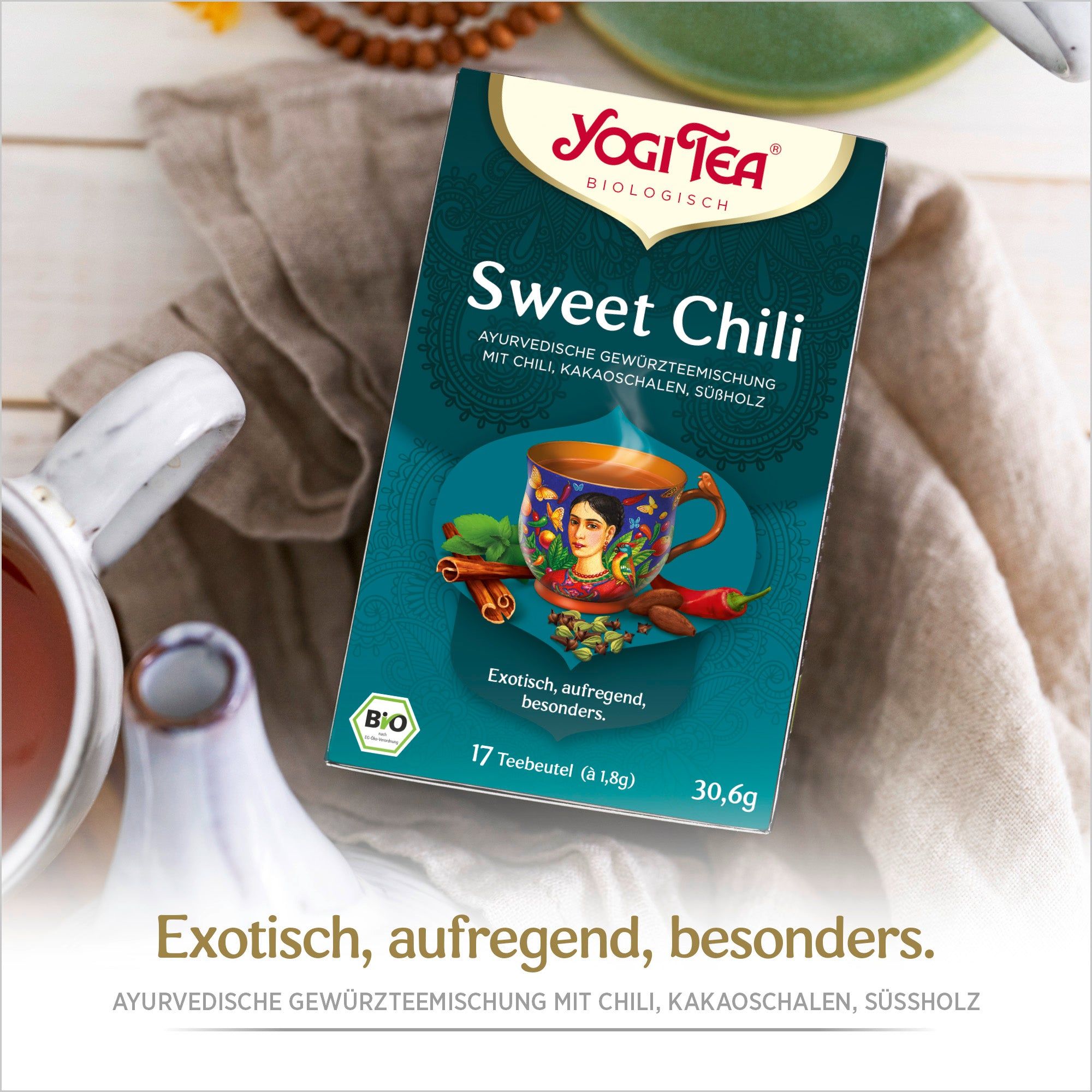 Yogi Tea Sweet Chili Bio Gewürztee Packung. Aufdrucke: Yogi Tea, Sweet Chili, 17 Teebeutel, Bio-Siegel. Auf Tischdecke.