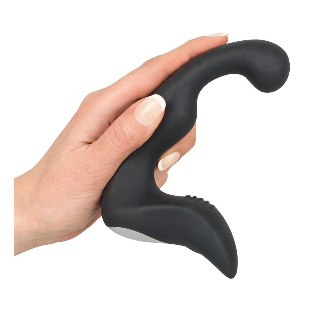 Schwarzes Wellness-Produkt in einer Hand gehalten. Abgerundete Spitze, gebogene Form. Unterseite weiß.