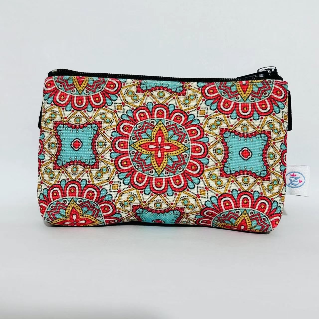 Tasche mit Mandala-Muster, Reißverschluss, kleines Etikett. Farbmuster: Rot, Türkis, Gelb. Schwarzer Reißverschluss.