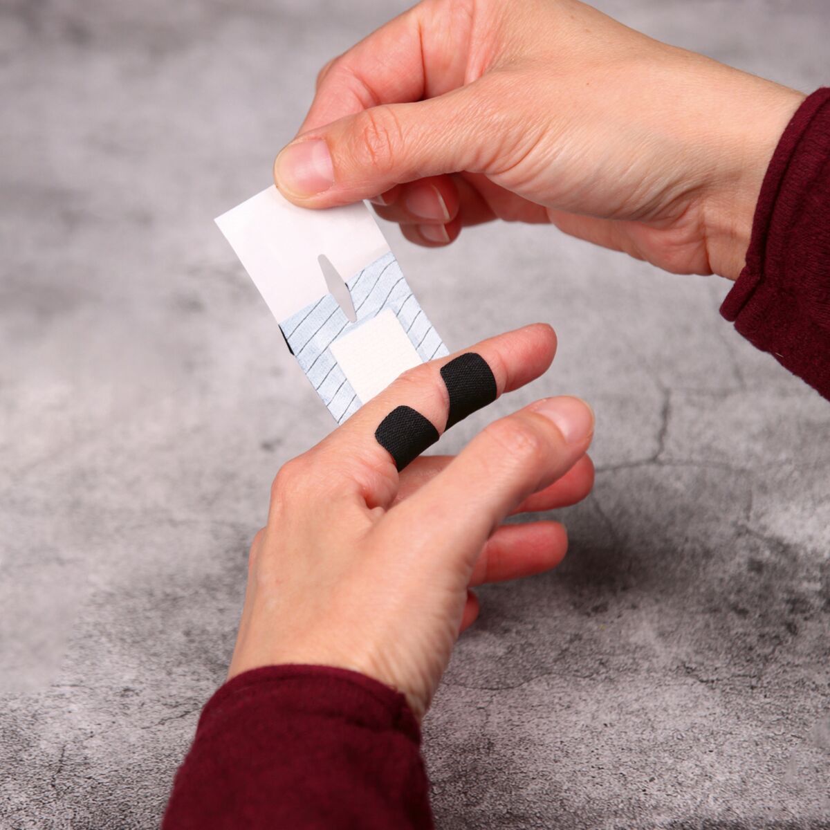 Person wendet ein schwarzes WERO PowerTex Fingergelenkpflaster auf den Finger an.