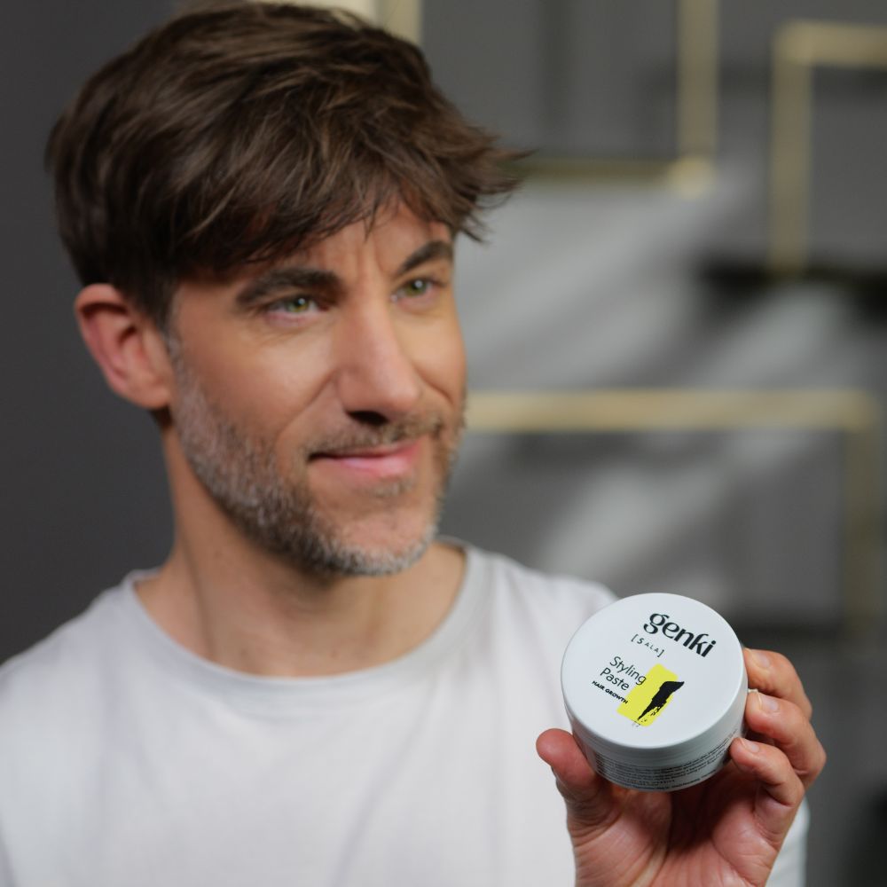 Mann hält Genki Styling Paste Dose. Grauer Deckel, schwarzer Schriftzug, gelber Farbfleck.