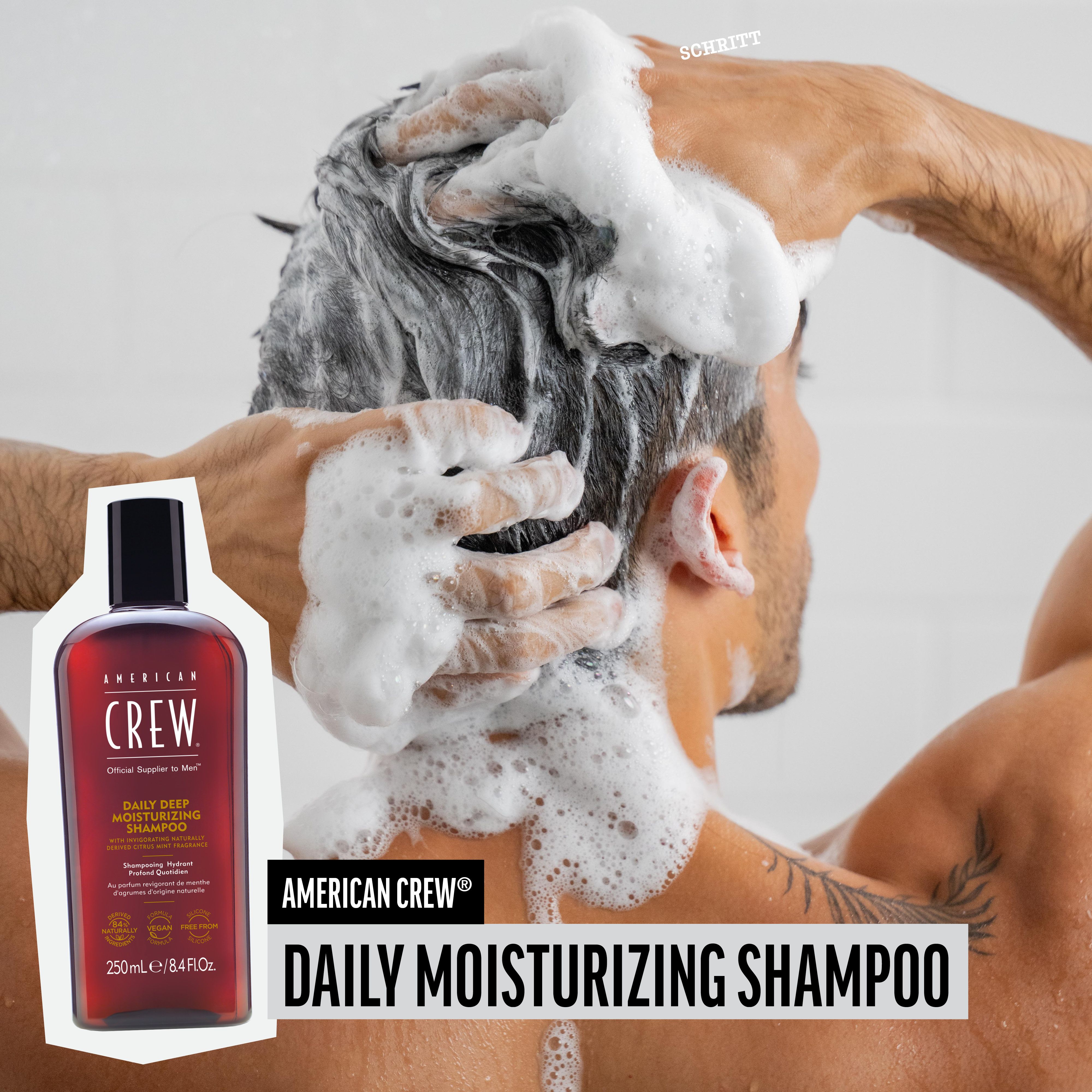 Mann wäscht sich die Haare mit Shampoo. AMERICAN CREW Daily Moisturizing Shampoo-Flasche im Bild.