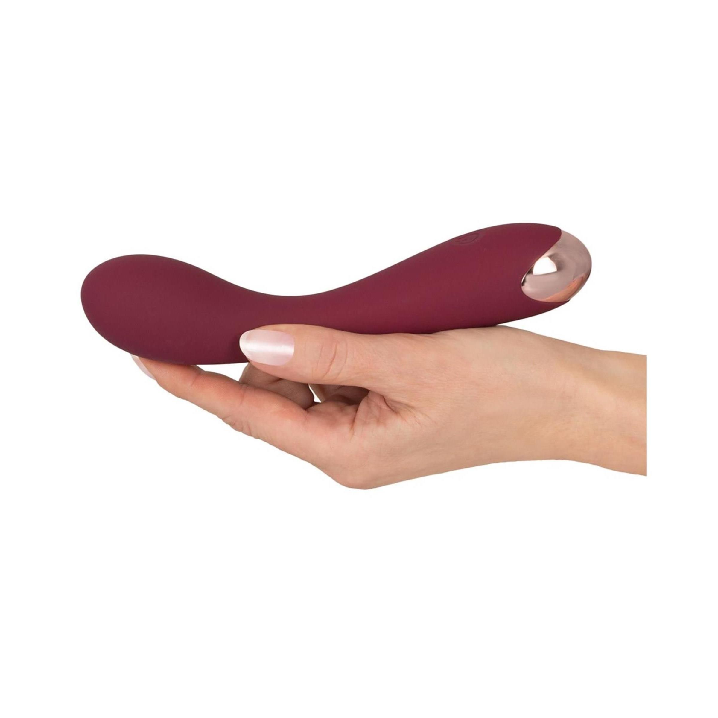 Burgunderfarbener Vibrator in einer Hand gehalten. Metallspitze sichtbar.