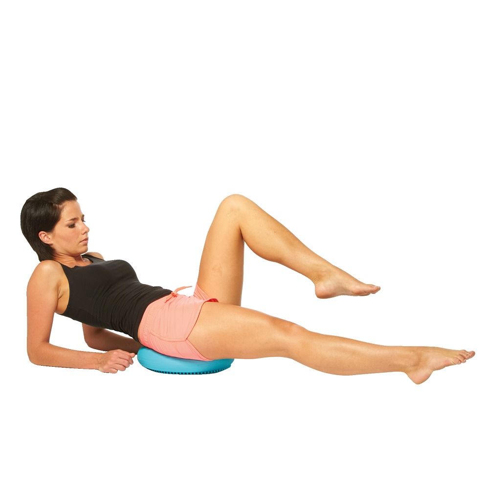 Frau liegt auf dem Boden und trainiert mit einem blauen Ballkissen. Kissen ist rund.