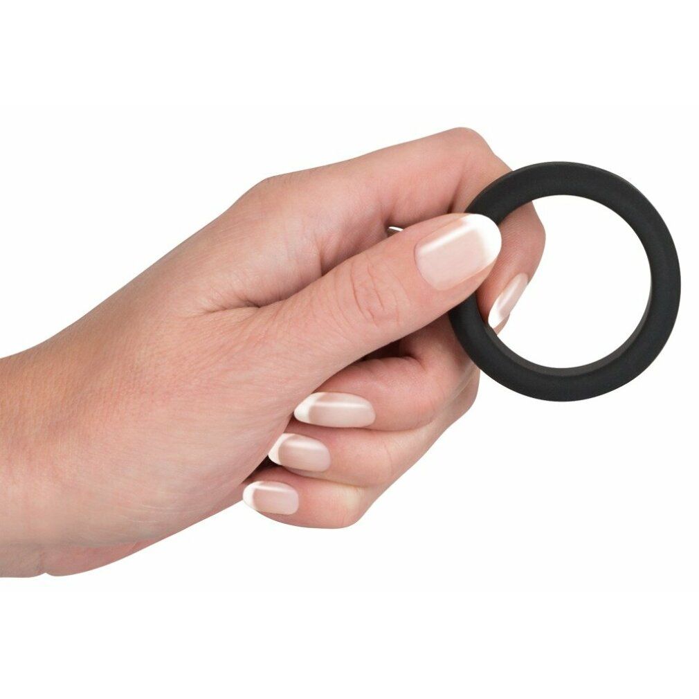 Hand hält schwarzen Penisring. Ringförmig, mit glatter Oberfläche.