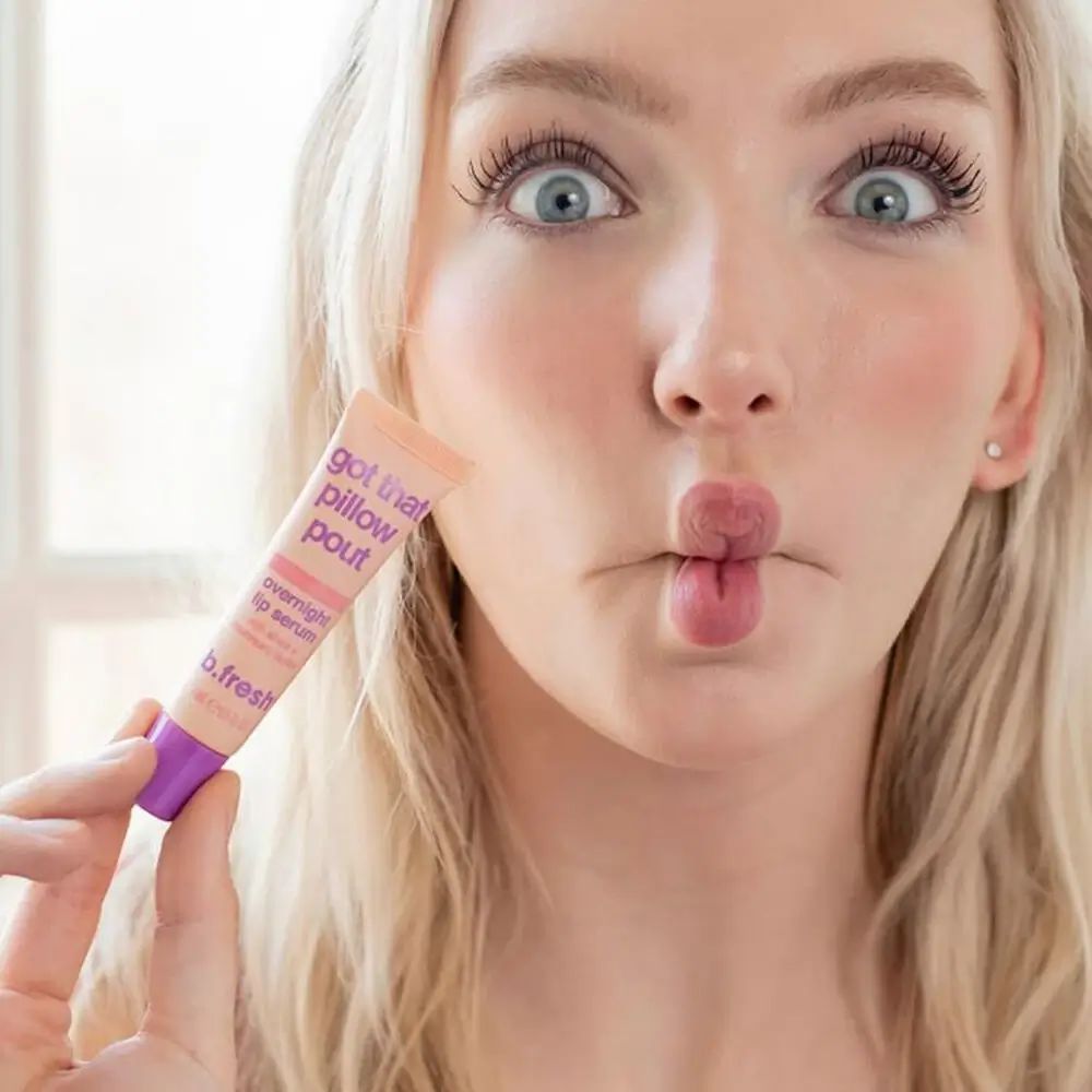 Frau hält Tube Overnight Lip Serum. Rosa Tube mit lila Verschluss. Aufschrift: Got that pillow pout, Overnight Lip Serum, b.fresh.
