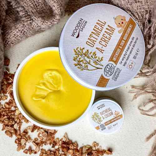 Geöffnete Dose mit gelber Creme, daneben Deckel und kleine Dose. Aufschrift: WOODEN SPOON, OATMEAL A-CREAM, ECO CERT.
