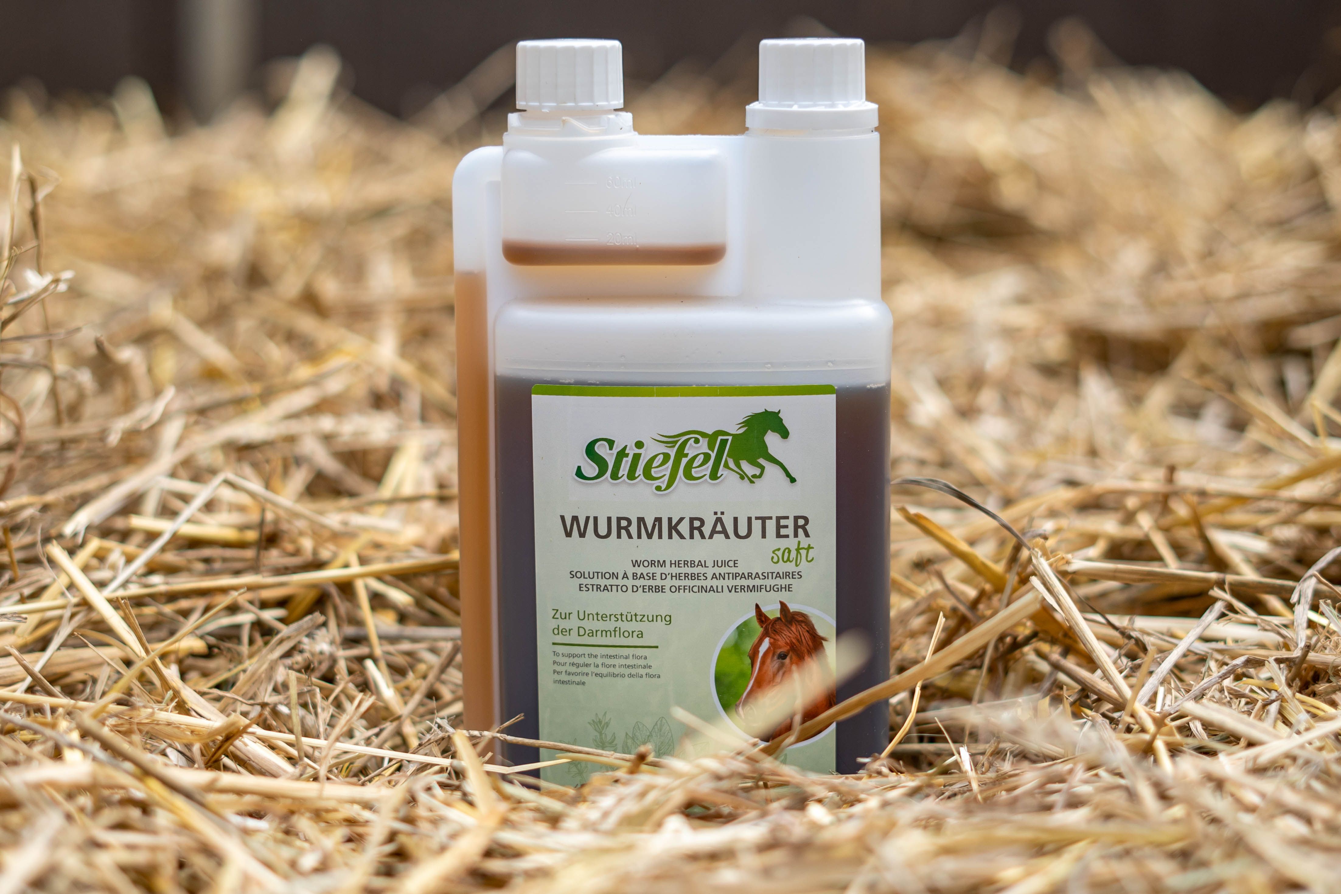 Doppelkammerflasche mit brauner Flüssigkeit. Aufschrift: Stiefel Wurmkräuter Saft. Auf Strohhalmen platziert.