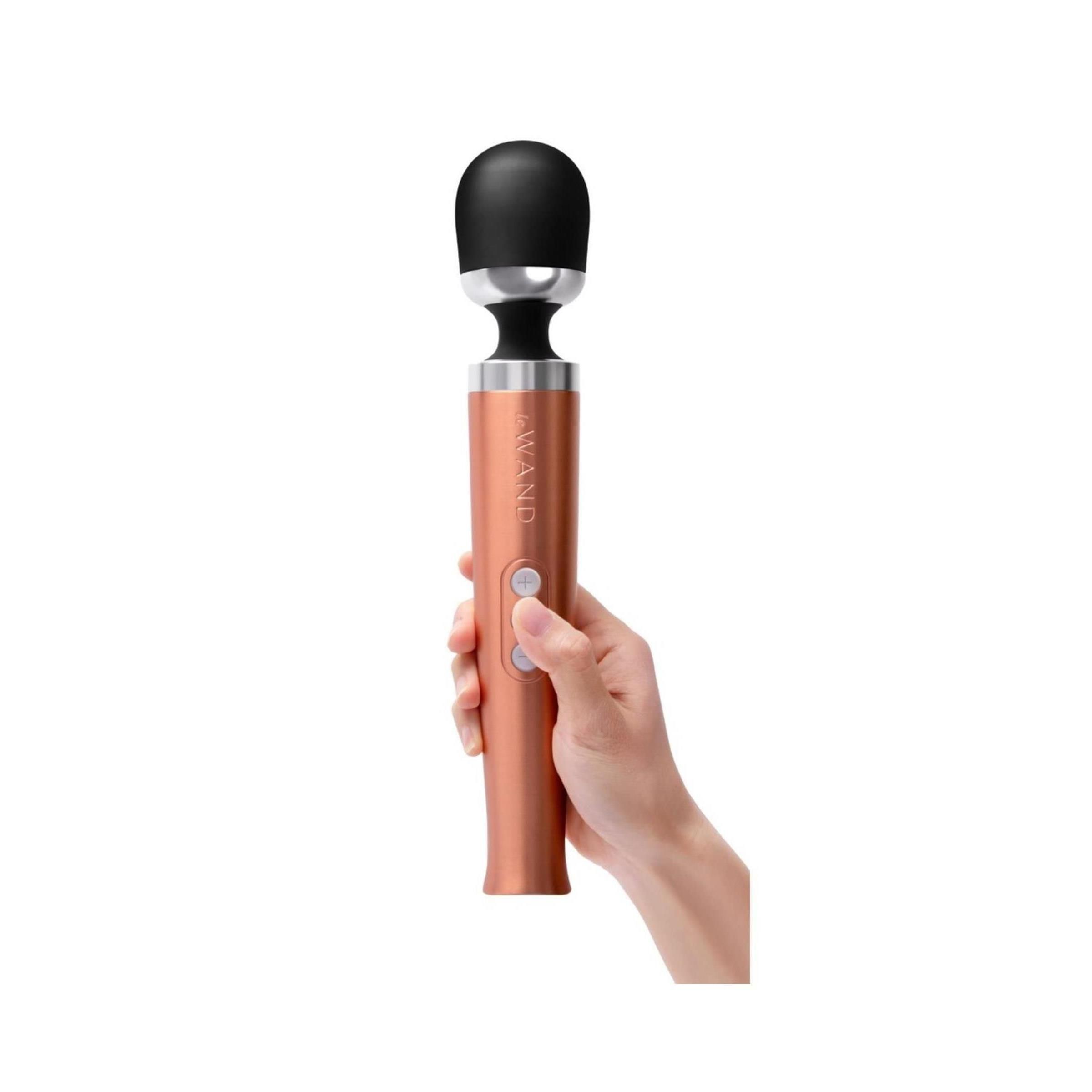 Hand hält roségoldfarbenes Massagegerät mit schwarzem Kopf. Drei Knöpfe sind sichtbar. Der Schriftzug "Le Wand" ist erkennbar.