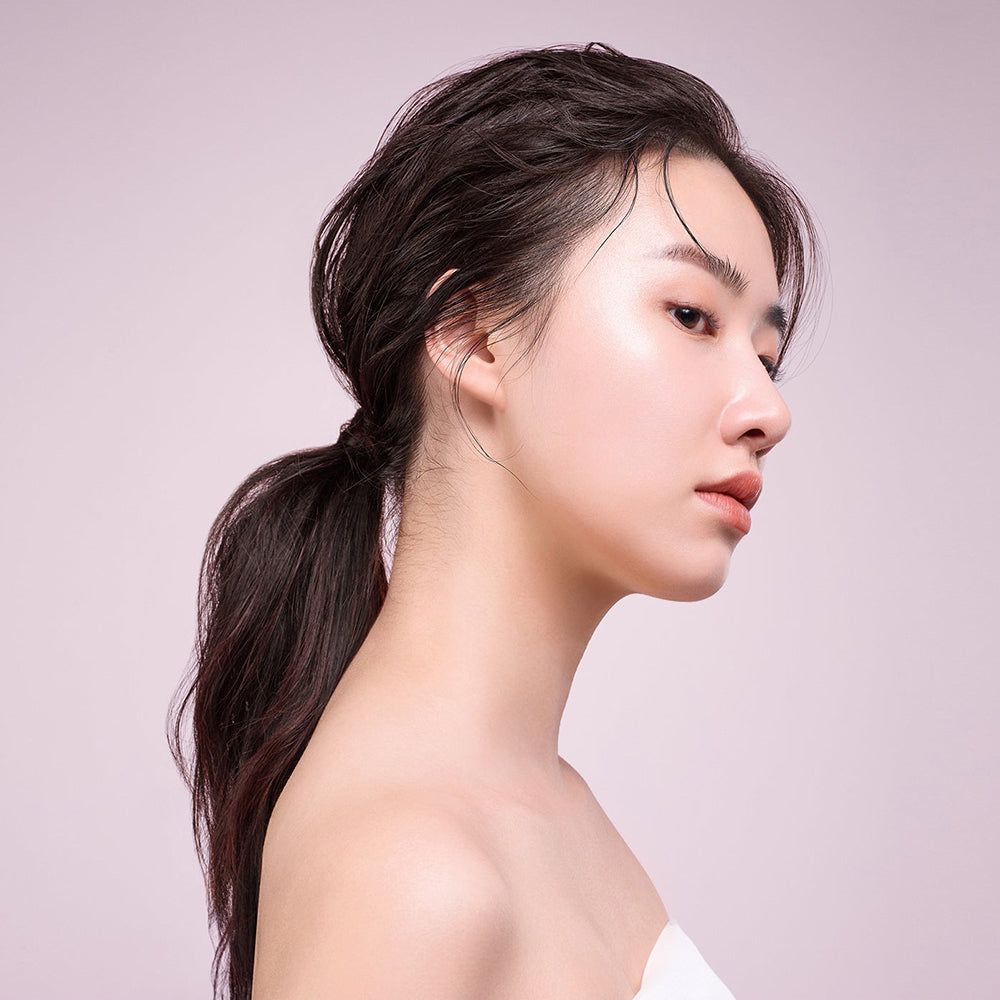 Profil einer Frau mit nassen Haaren, die zu einem Pferdeschwanz gebunden sind. Sie trägt ein weißes Handtuch.