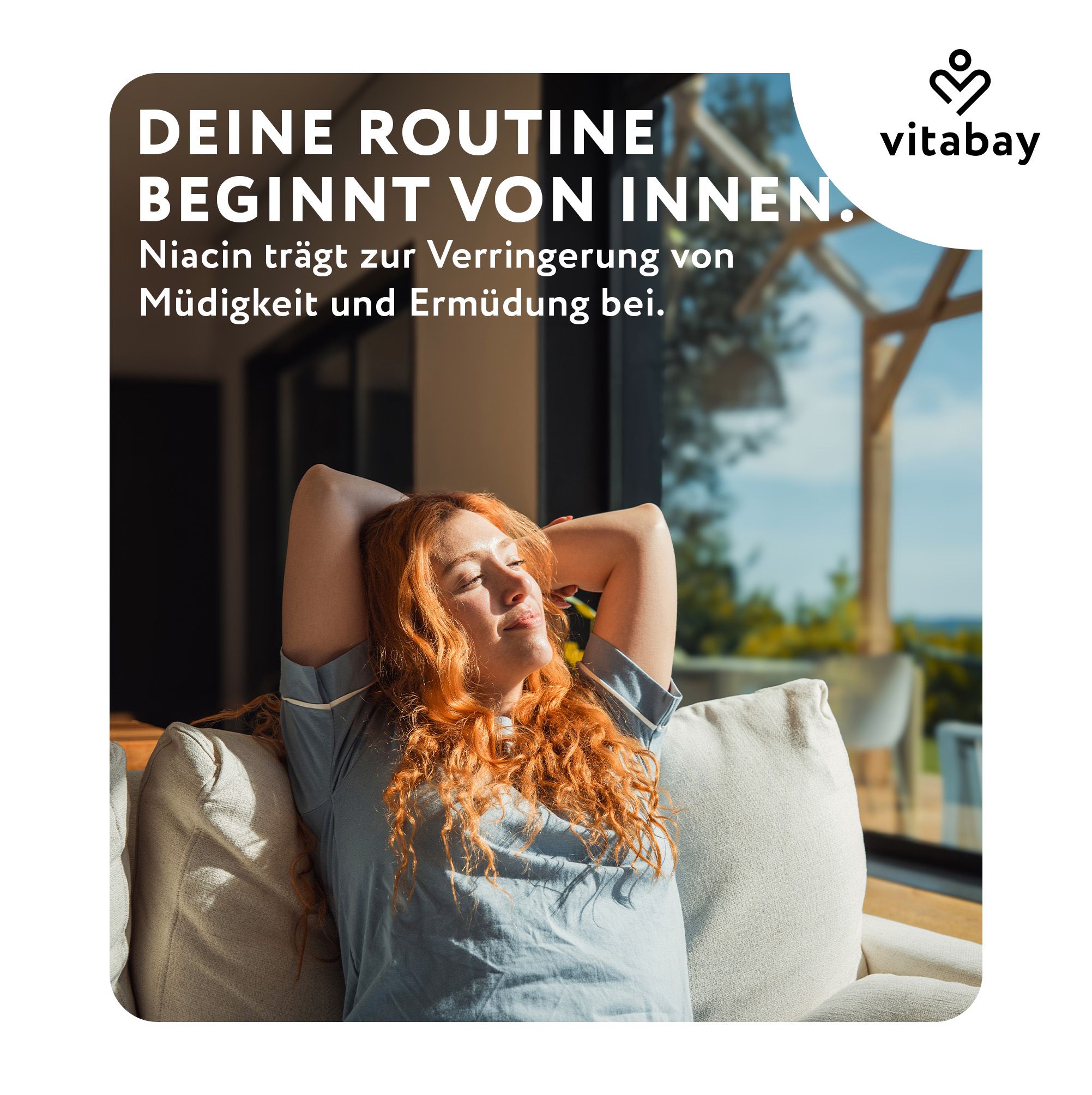 Frau mit roten Haaren entspannt auf einem Sofa, Sonne scheint.