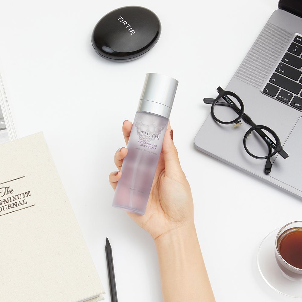 Hand hält TIRTIR Collagen Core Glow Essence neben einem Notizbuch und einer Brille.