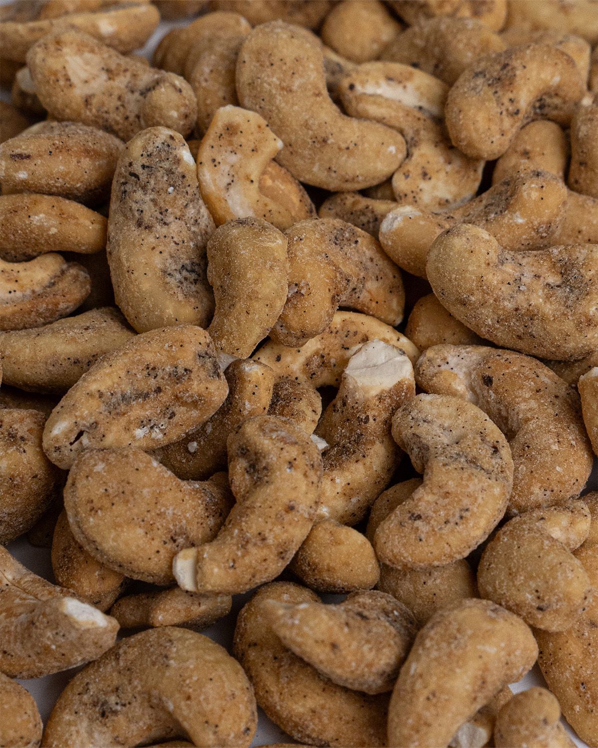 Nahaufnahme von Cashewkernen. Die Kerne sind mit Gewürzen bedeckt.