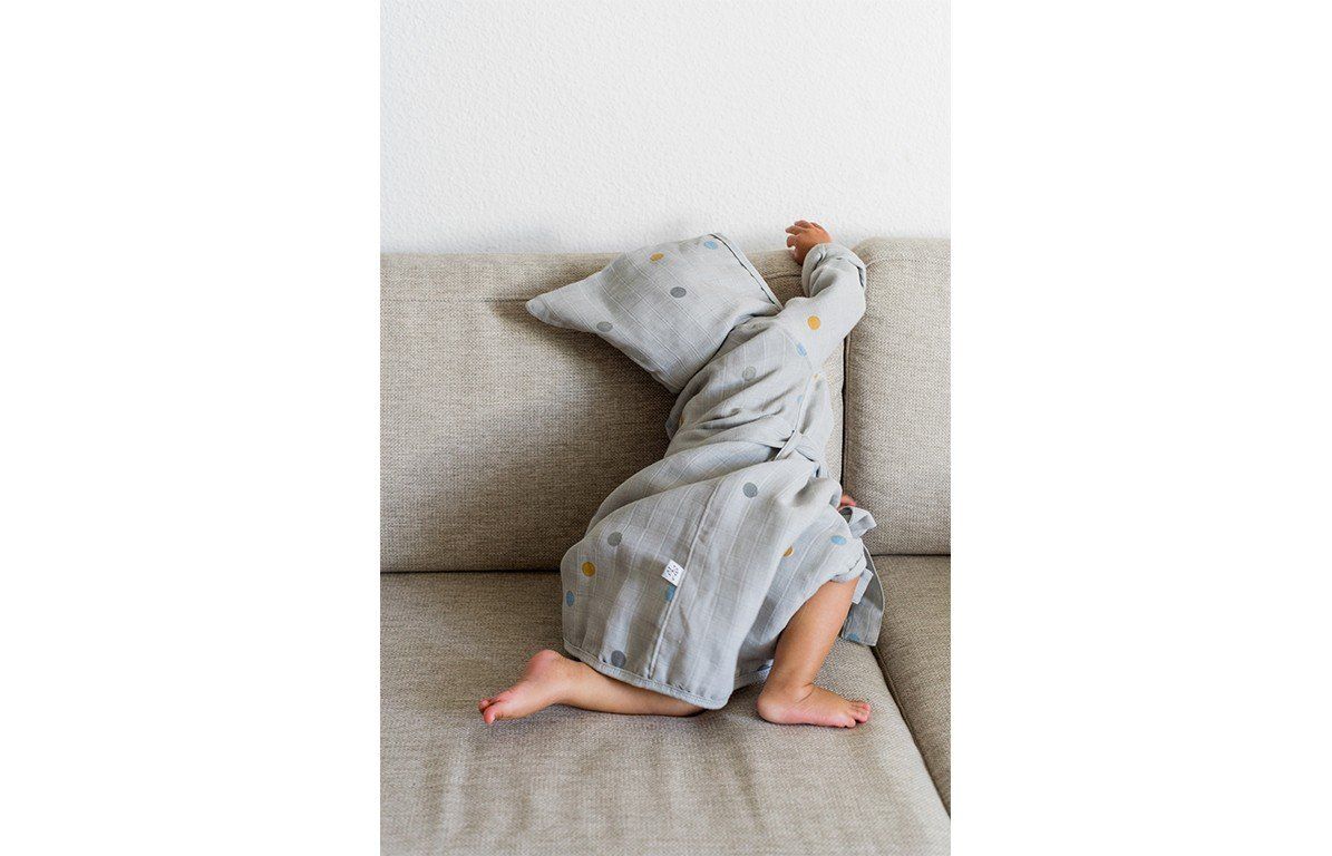 Kind sitzt auf einem Sofa und trägt einen grauen Bademantel mit Kapuze und Punkten. Kind bedeckt sich.