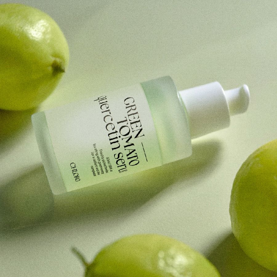 Serumflasche mit Pumpverschluss, umgeben von grünen Zitronen. Aufschrift: GREEN TOMATO quercetin serum. Marke: CHLORO.