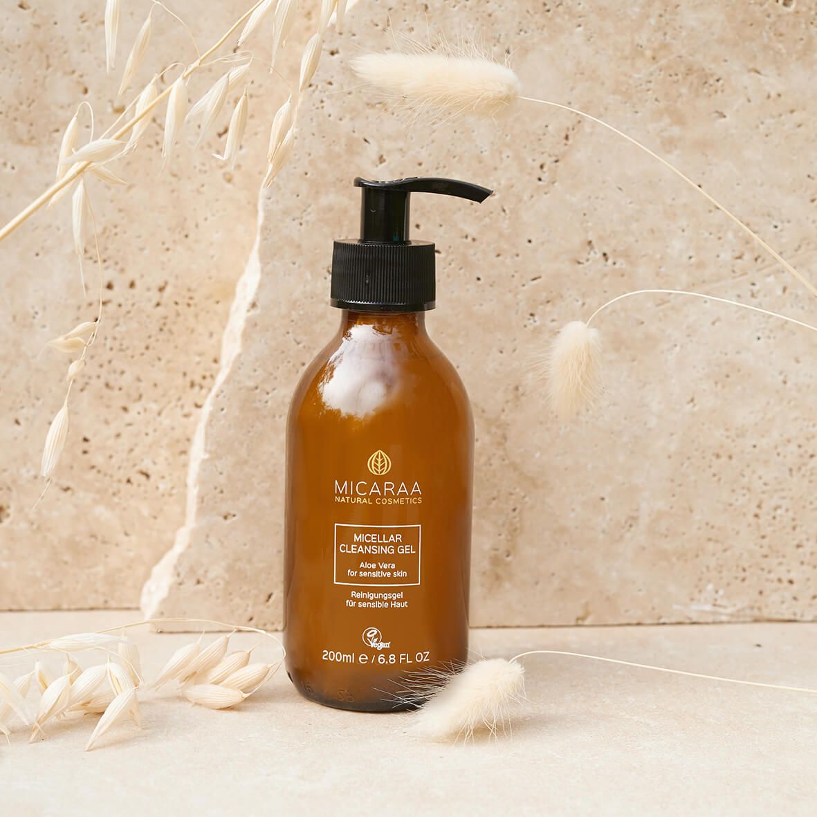 Braune Flasche mit schwarzem Pumpverschluss. Aufschrift: MICARAA Micellar Cleansing Gel, Aloe Vera für empfindliche Haut. Vegan-Siegel. Dekoration.