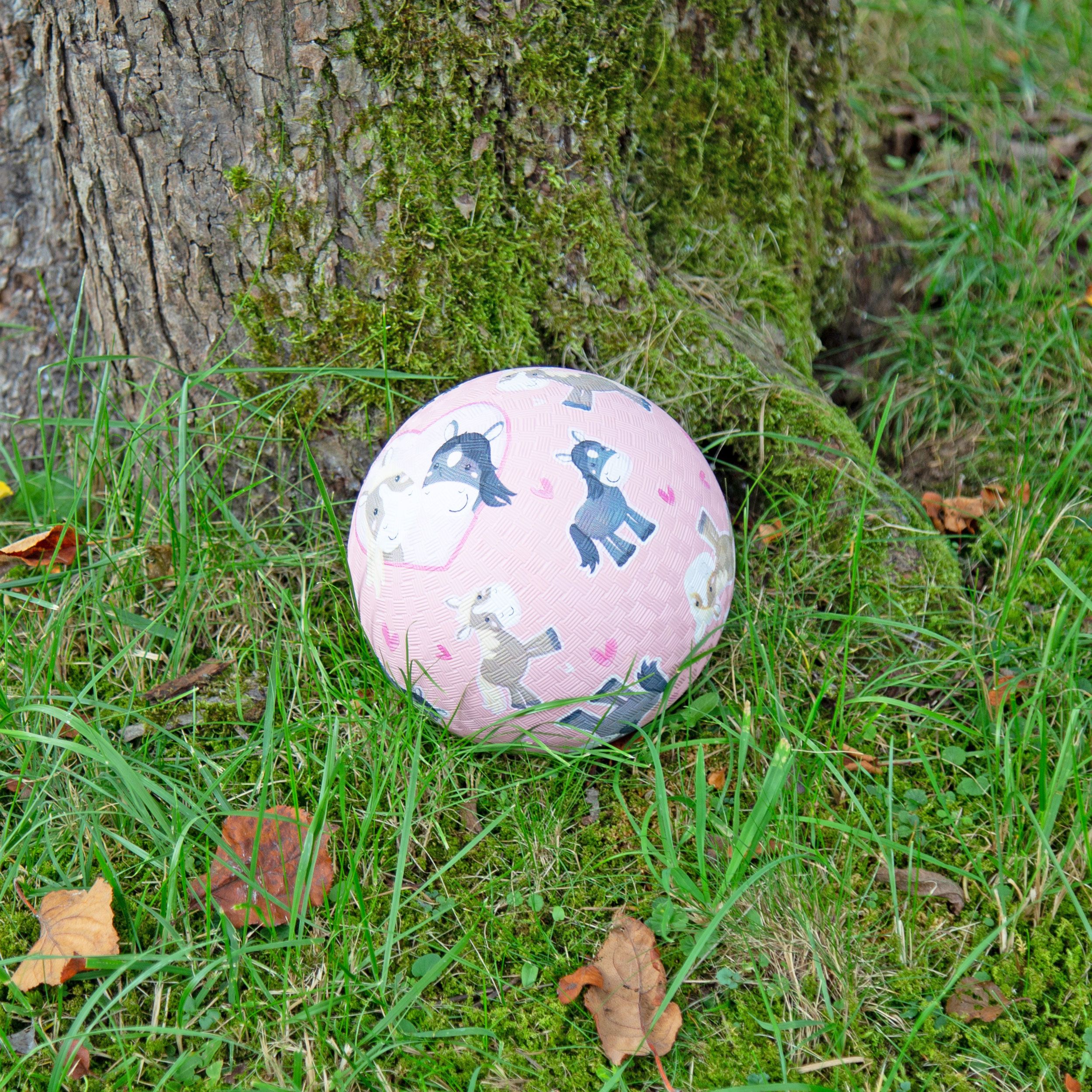Rosa Kautschuk Ball mit Pony-Motiven auf Gras. Der Ball hat eine strukturierte Oberfläche.